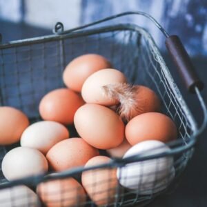 A close-up of farm fresh eggs in a metal basket, featuring a delicate feather for a rustic touch.